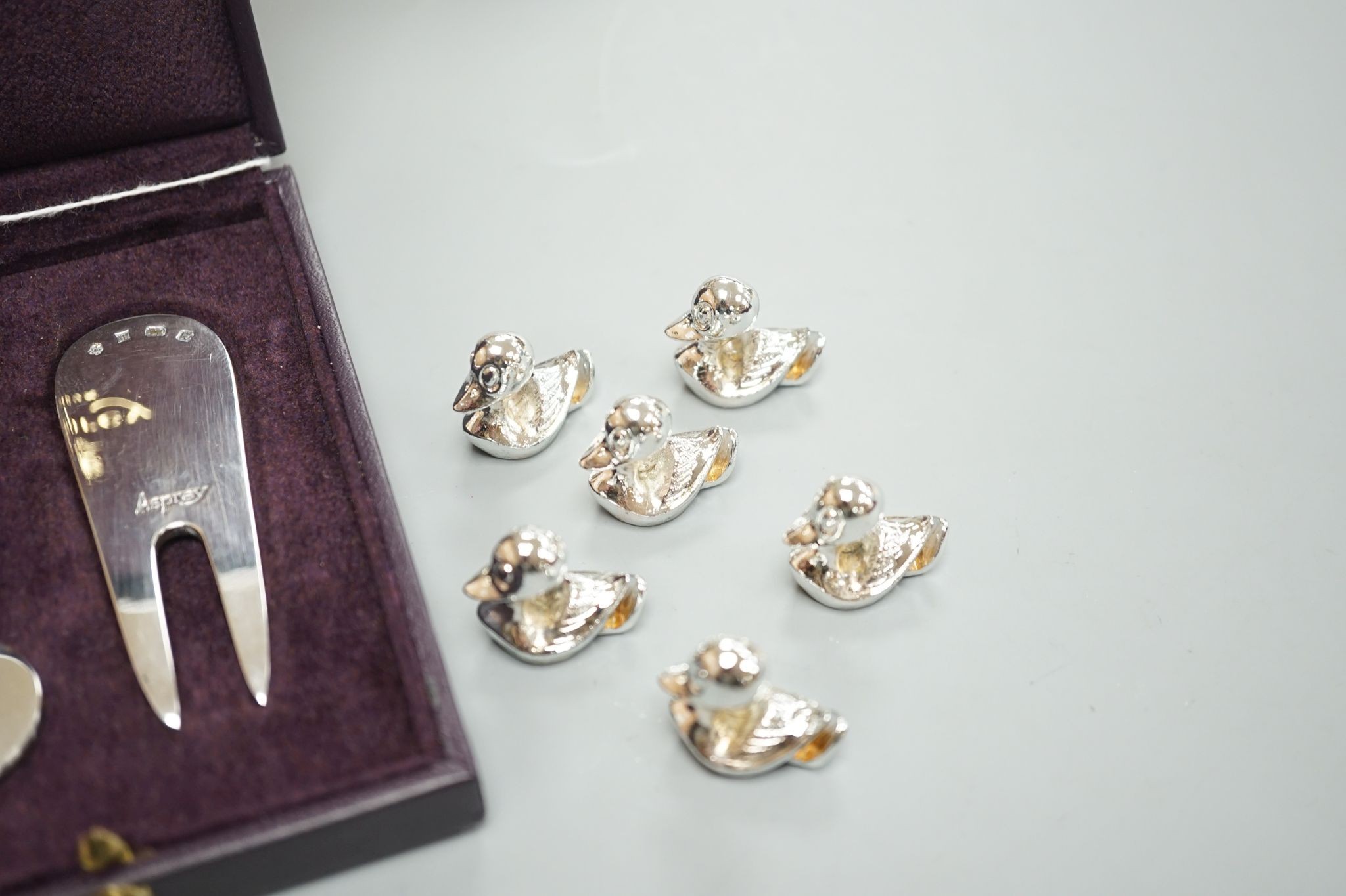A modern Asprey cased silver golfer's companion set, comprising a tee, marker and pitch mark repairer, together with a set of six metal duck menu holders.